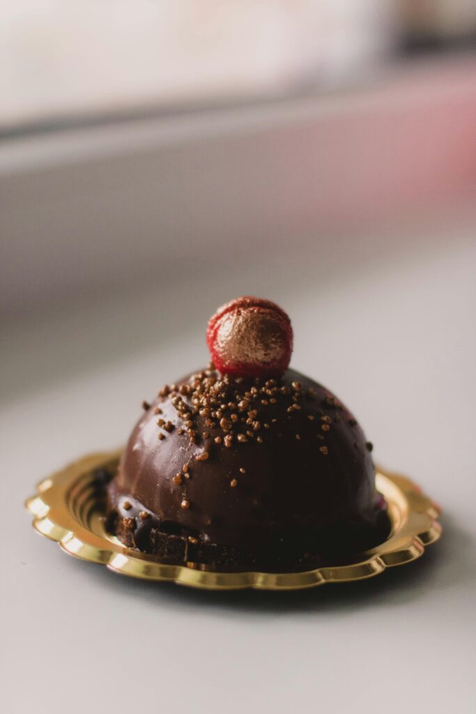 Luxurious chocolate dessert on gold plate with red candy topping, perfect for indulgence.